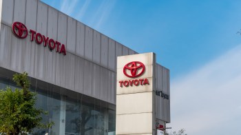 A Toyota dealership sign displayed outside a modern building against a clear blue sky.
