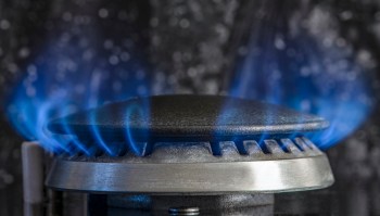 A close-up of a gas stove burner with blue flames ignited.