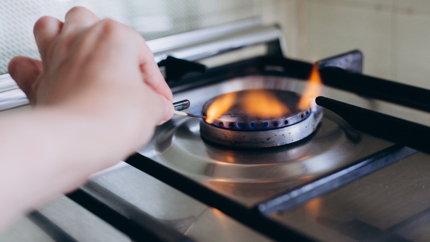 A hand striking a match near a gas stove burner with a small flame igniting.