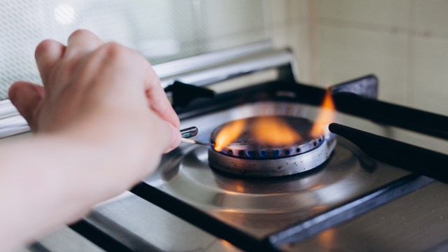A hand striking a match to ignite a gas burner on a stove, with flames starting to rise.