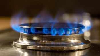 A close-up of a gas stove burner with blue flames flickering around a metallic surface.