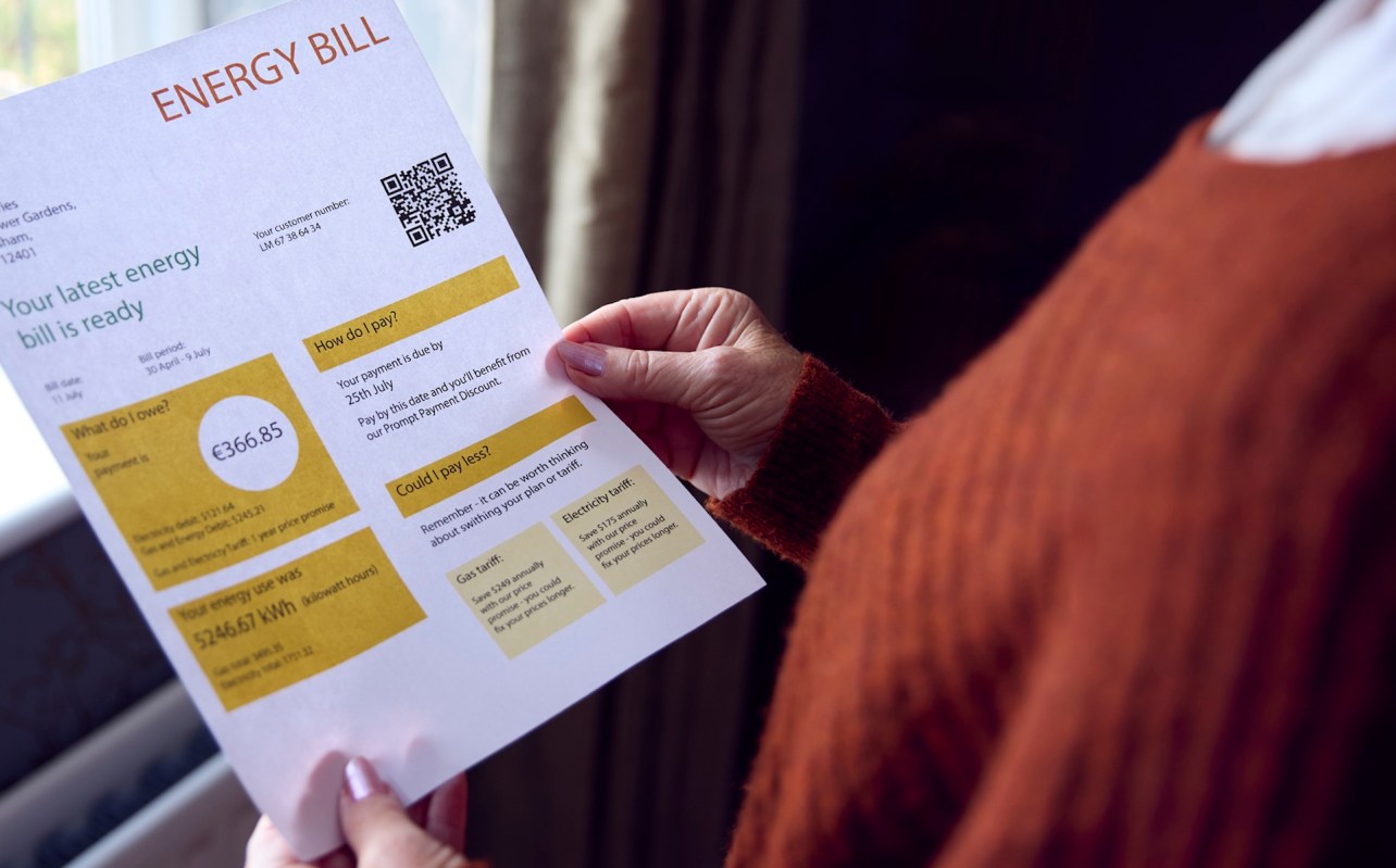 A person holding an energy bill document with details on payment and usage in a home setting.