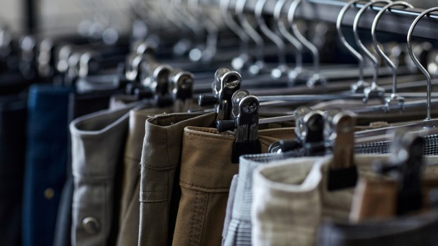 A close-up of various pairs of pants hanging on clips in a display of secondhand clothing store.
