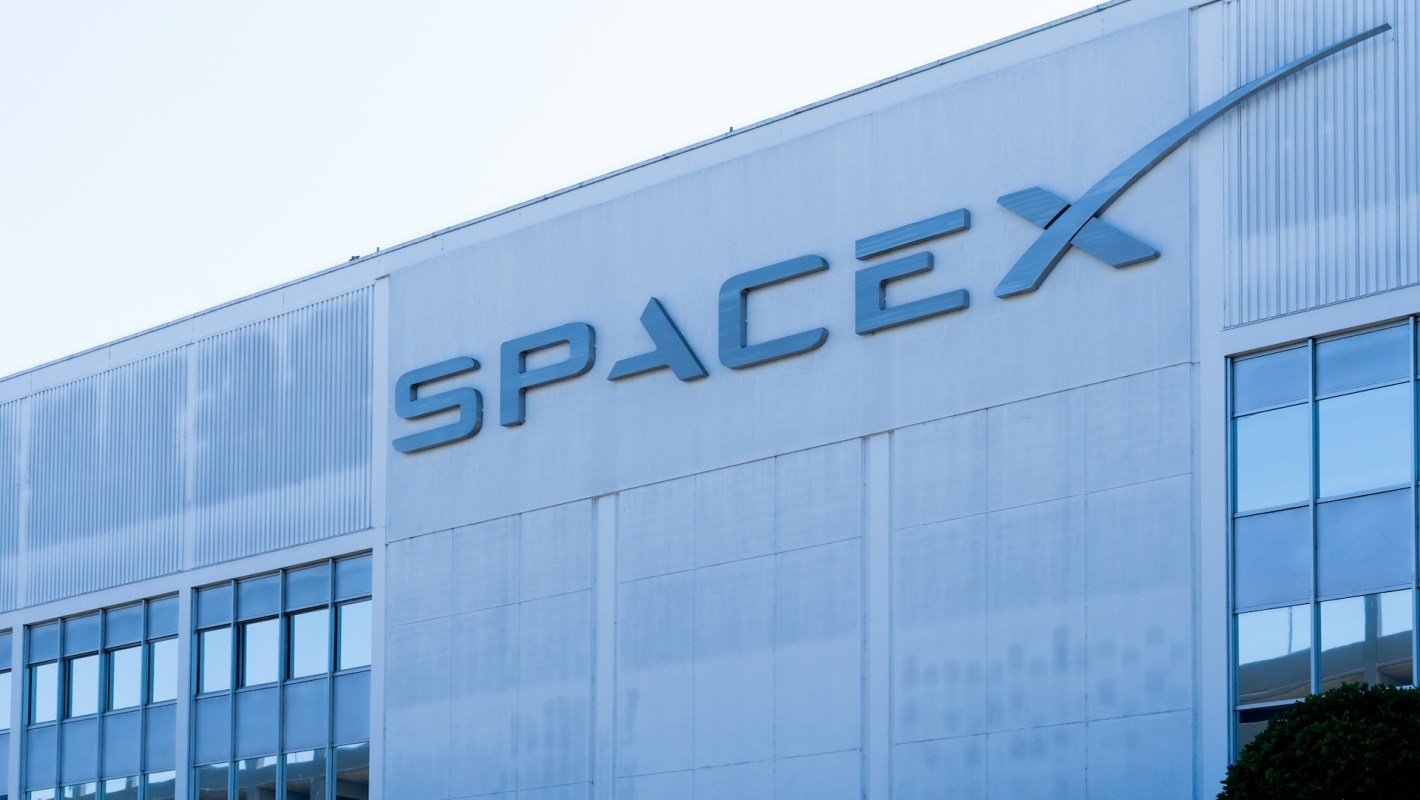 The SpaceX logo prominently displayed on the side of a building under clear blue skies.