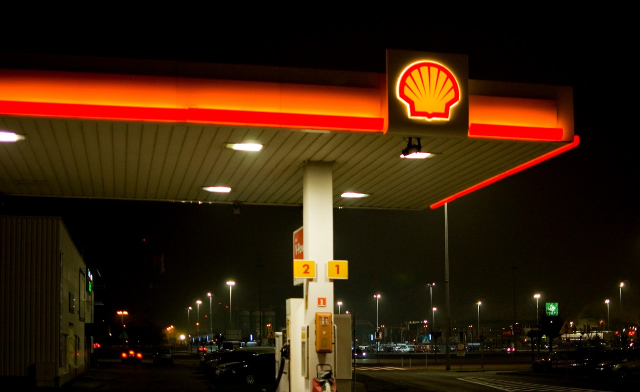 A Shell gas station illuminated at night with visible fuel pumps and surrounding parking lot lights.