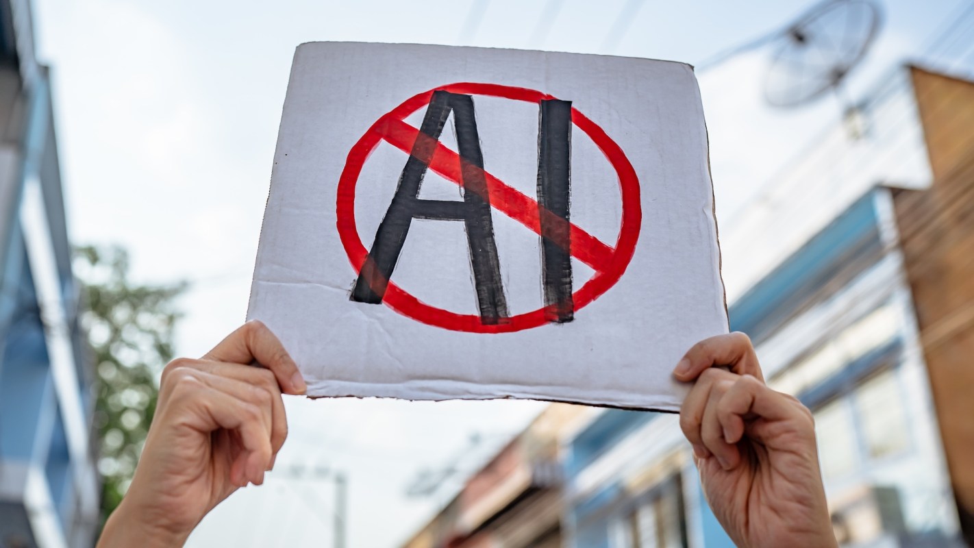 A protestor holds a sign with "AI" crossed out in red.