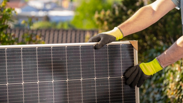 A person wearing gloves installs a solar panel in a sunny outdoor setting.