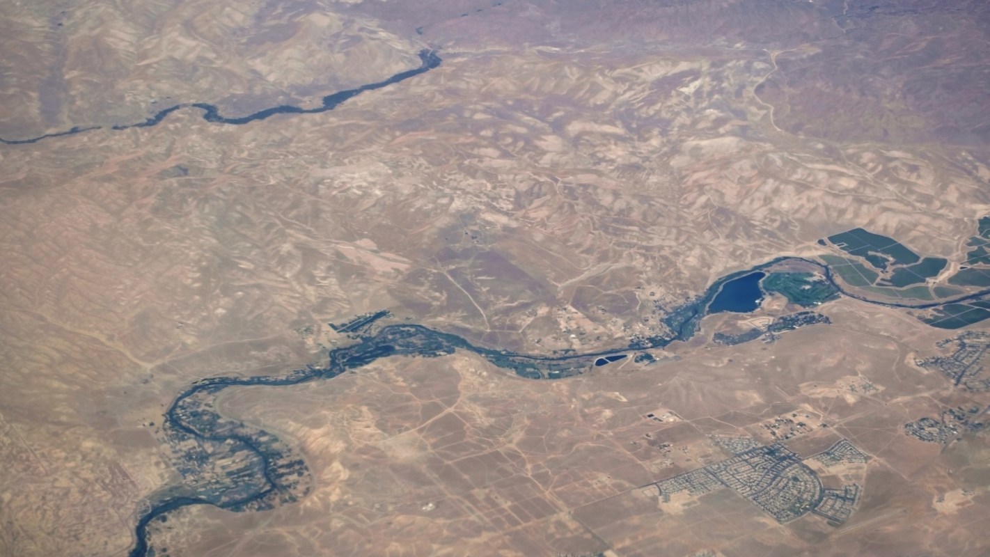 Aerial view of a winding river through arid land with patches of greenery and small settlements.