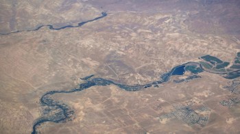 Aerial view of a winding river through arid land with patches of greenery and small settlements.