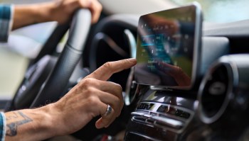 A close-up of a hand interacting with a car's touchscreen display while driving.