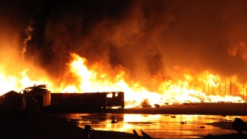 A large fire engulfing debris and structures, with flames illuminating the dark sky.
