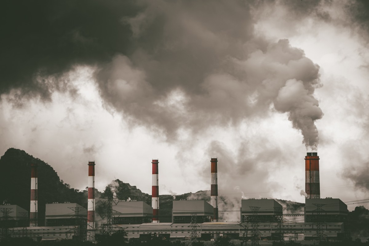 A coal power plant with smokestacks releasing thick smoke against a backdrop of dark, cloudy skies.