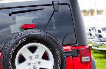 A close-up view of a Jeep Wrangler's rear tire and tailgate, featuring a red and black color scheme.