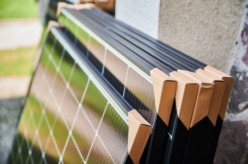 A close-up of stacked solar panels with protective corners, set against a blurred outdoor background.