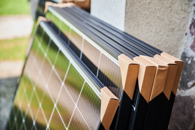 A close-up of stacked solar panels with protective corners, set against a blurred outdoor background.
