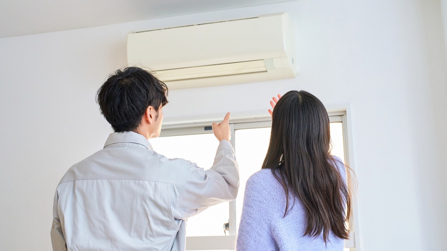 A man and woman are pointing toward a mini-split unit while standing near a window.