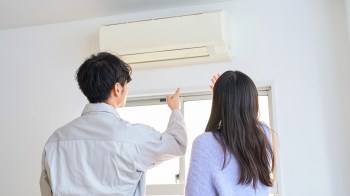 A man and woman are pointing toward a mini-split unit while standing near a window.