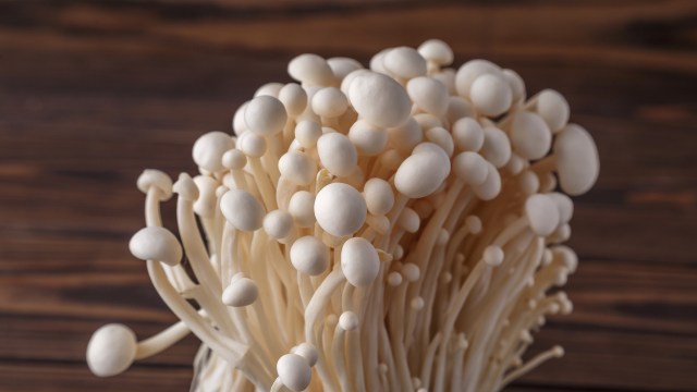 A close-up of delicate white enoki mushrooms on a wooden surface.