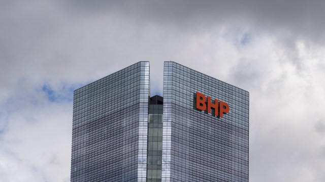 A close-up view of a modern glass building with the "BHP" logo against a cloudy sky.