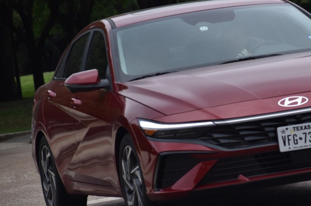 A red Hyundai sedan with a modern design parked on a street surrounded by green trees.