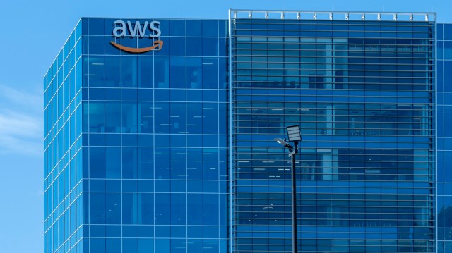 A close-up of a modern office building with "AWS" and Amazon's logo prominently displayed on the glass facade.
