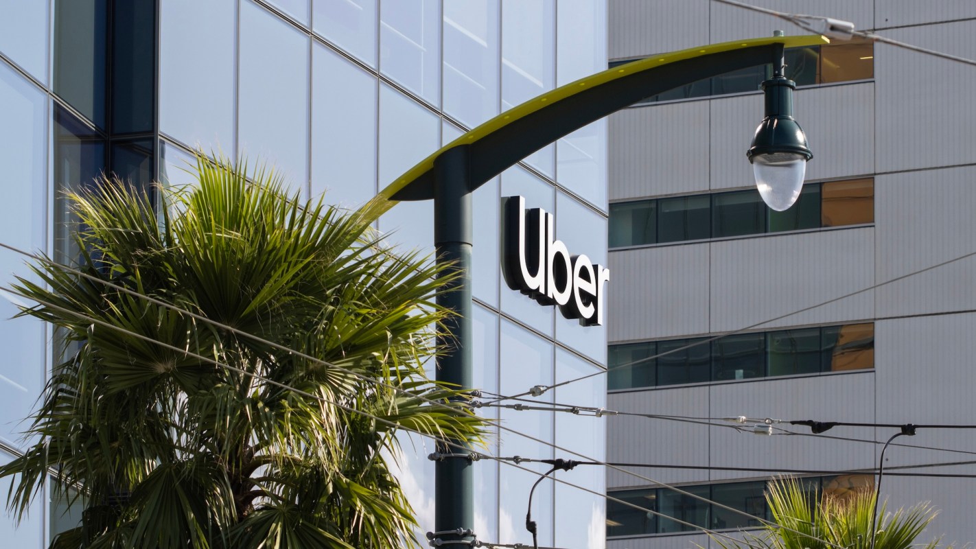 An Uber sign on a glass building near a palm tree.