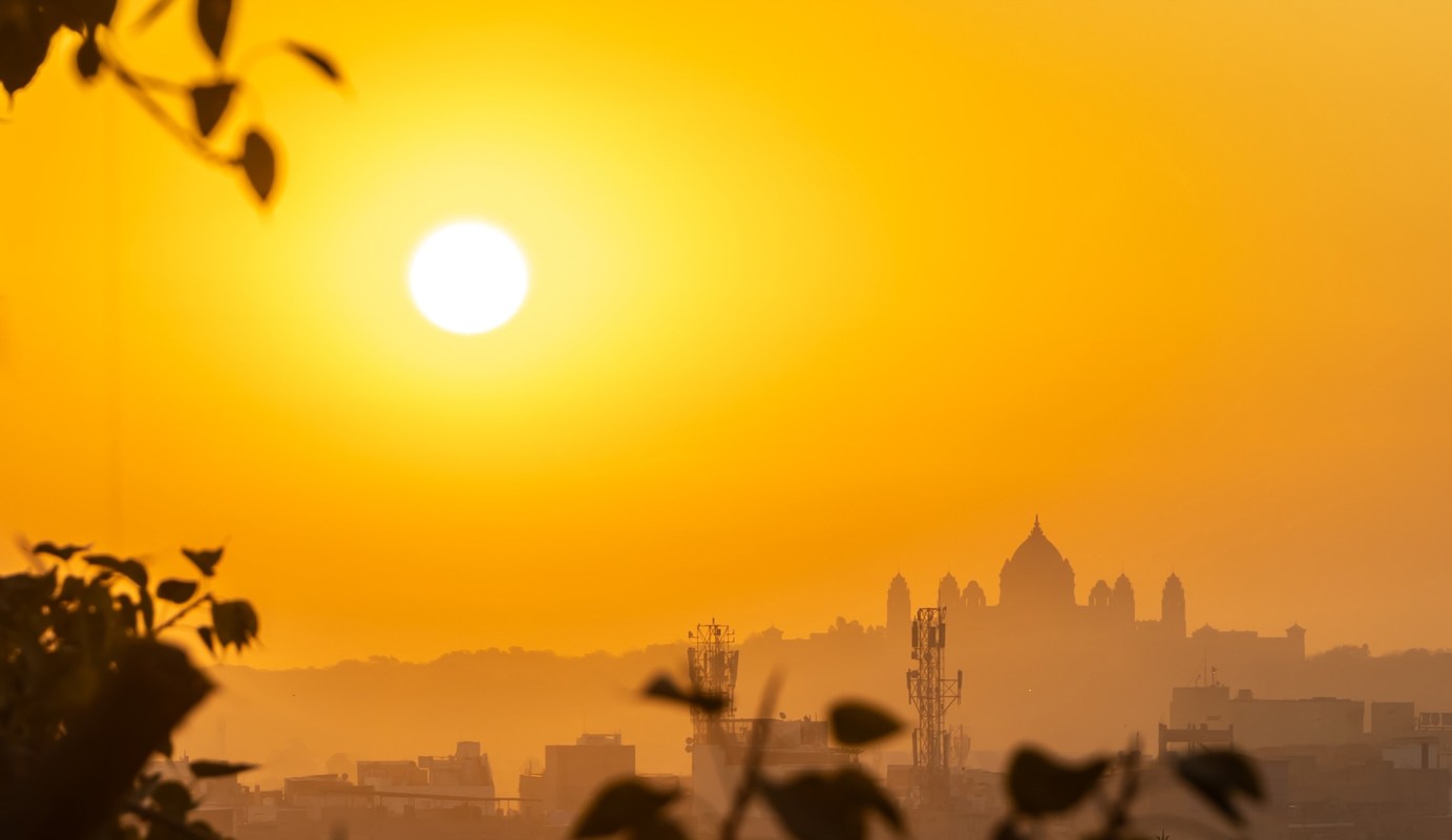 A bright orange sunset silhouetting buildings and trees against a hazy skyline.