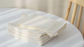 A neatly folded stack of cream-colored fabric towels on a white table with soft shadows.