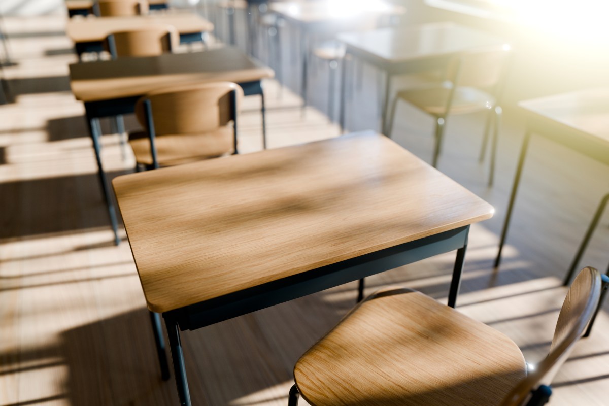 An empty classroom with wooden desks and chairs, illuminated by natural light.