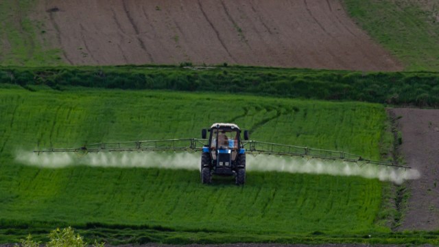 A tractor sprays chemicals over a lush green field with freshly cultivated soil in the background.