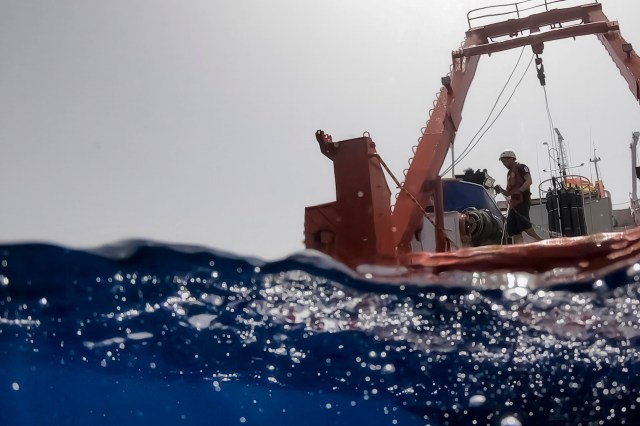 A view of an ocean surface with a ship and crew member visible above the waterline.