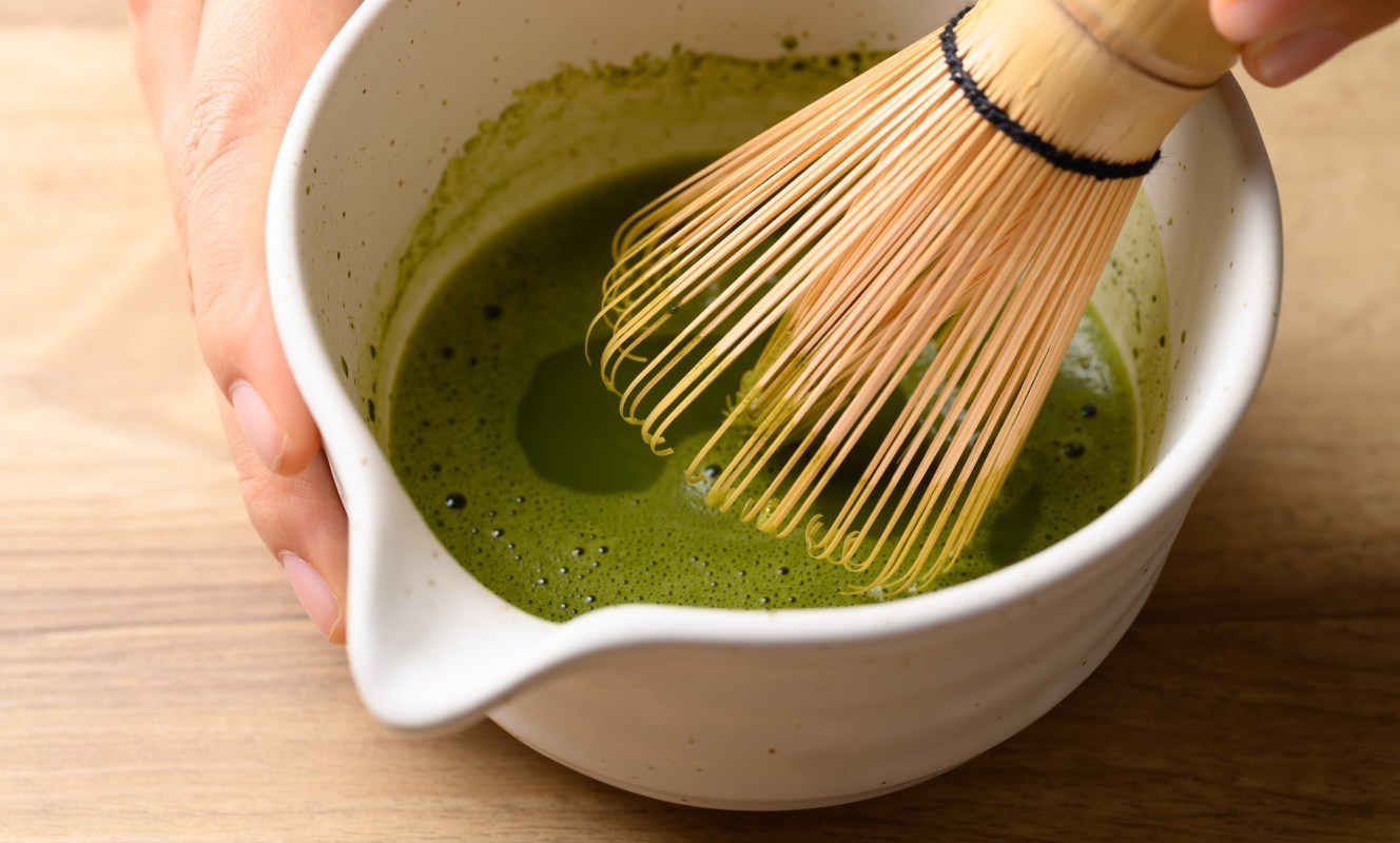 A hand whisking matcha tea in a ceramic container.
