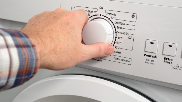 A hand adjusting the temperature dial on a washing machine displaying various wash cycle settings.
