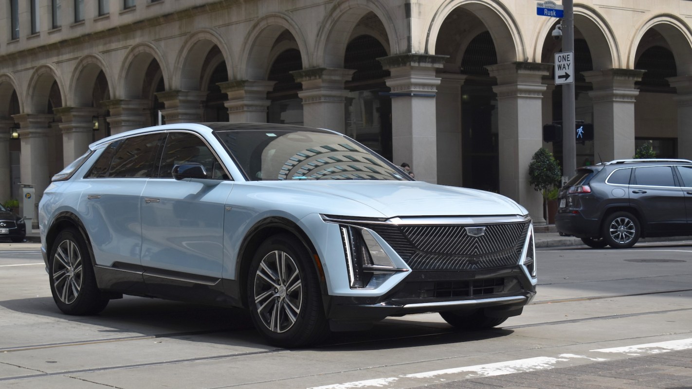 A light blue Cadillac SUV parked on an urban street with arched architecture in the background.