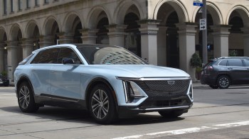 A light blue Cadillac SUV parked on an urban street with arched architecture in the background.