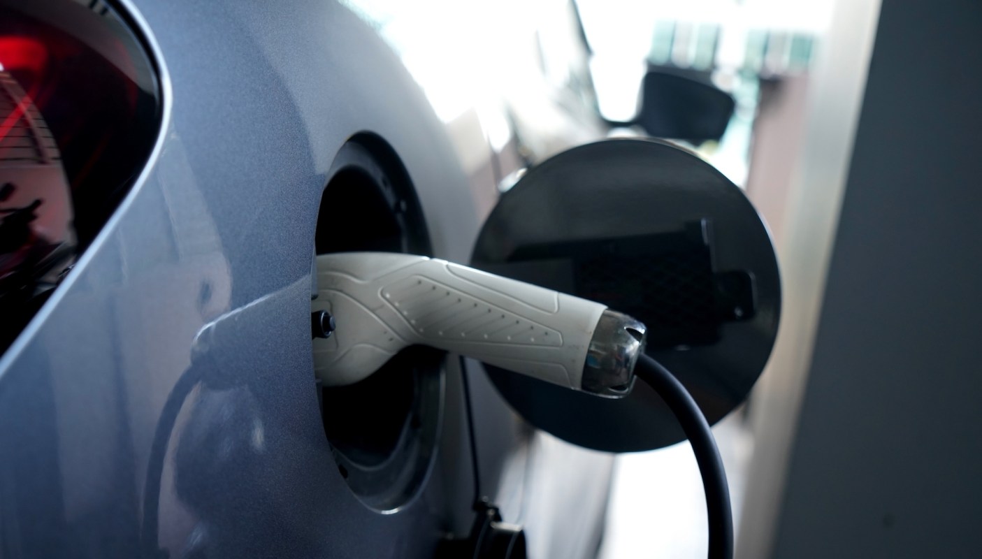 An electric car with a white charging cable in its port.