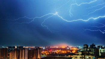 A dramatic lightning storm illuminates a city skyline at night.