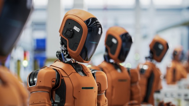 A row of futuristic orange robots with glossy black visors in a modern industrial setting.
