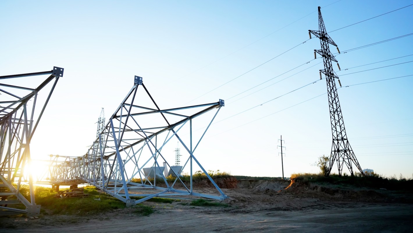 A construction site featuring a large steel power transmission tower and additional supporting structures at sunset.