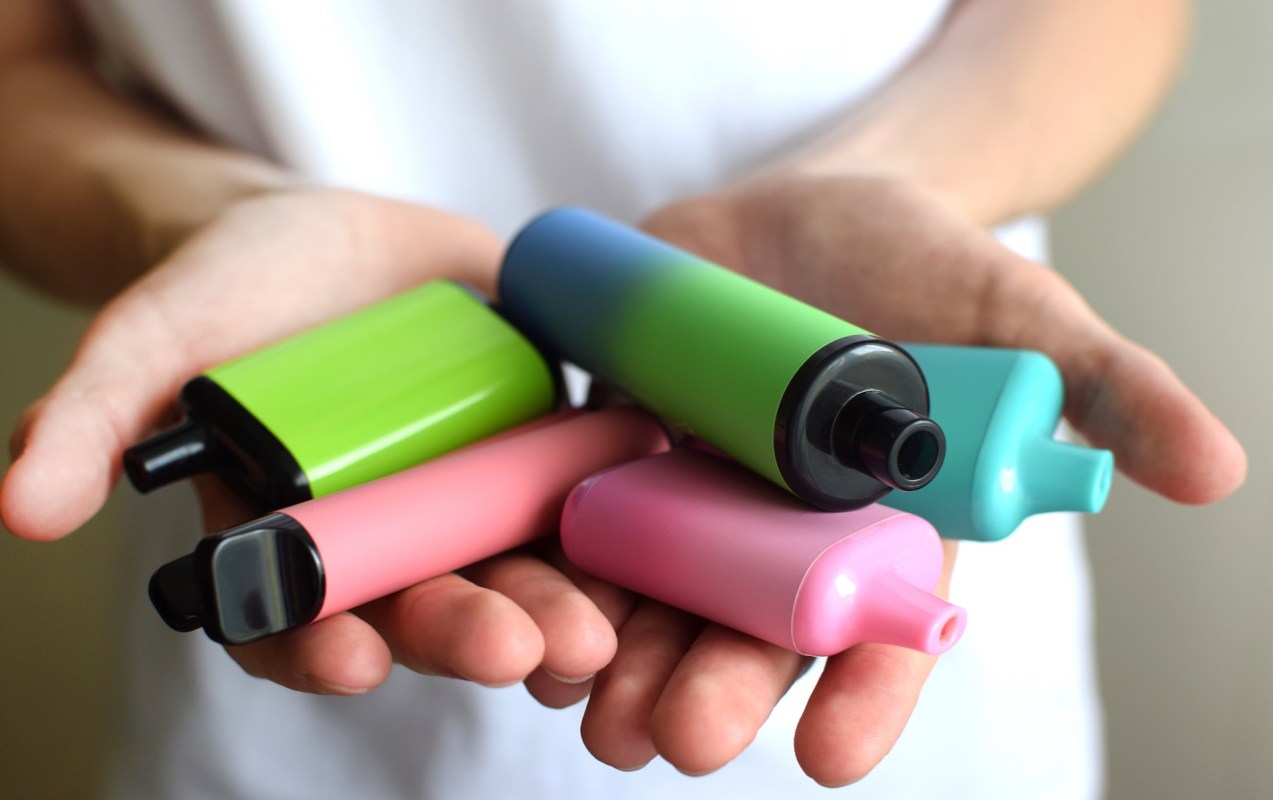 A person holds a variety of vapes in their hands.