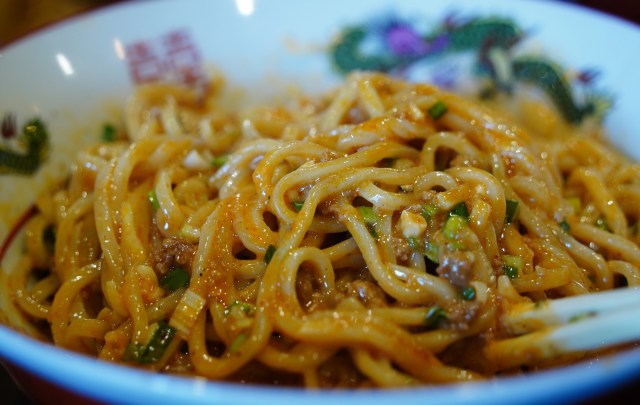 A bowl of noodles mixed with sauce and garnished with green onions.