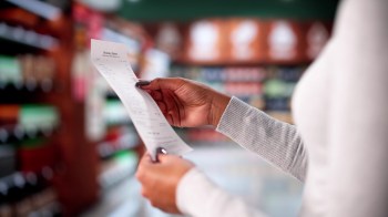 A person holds a grocery store receipt in a store aisle with products in the background.