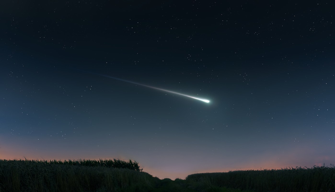 A bright comet streaks across a star-filled night sky above a dark landscape.