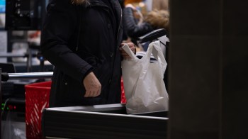 A person is placing a white plastic bag on a grocery checkout counter.