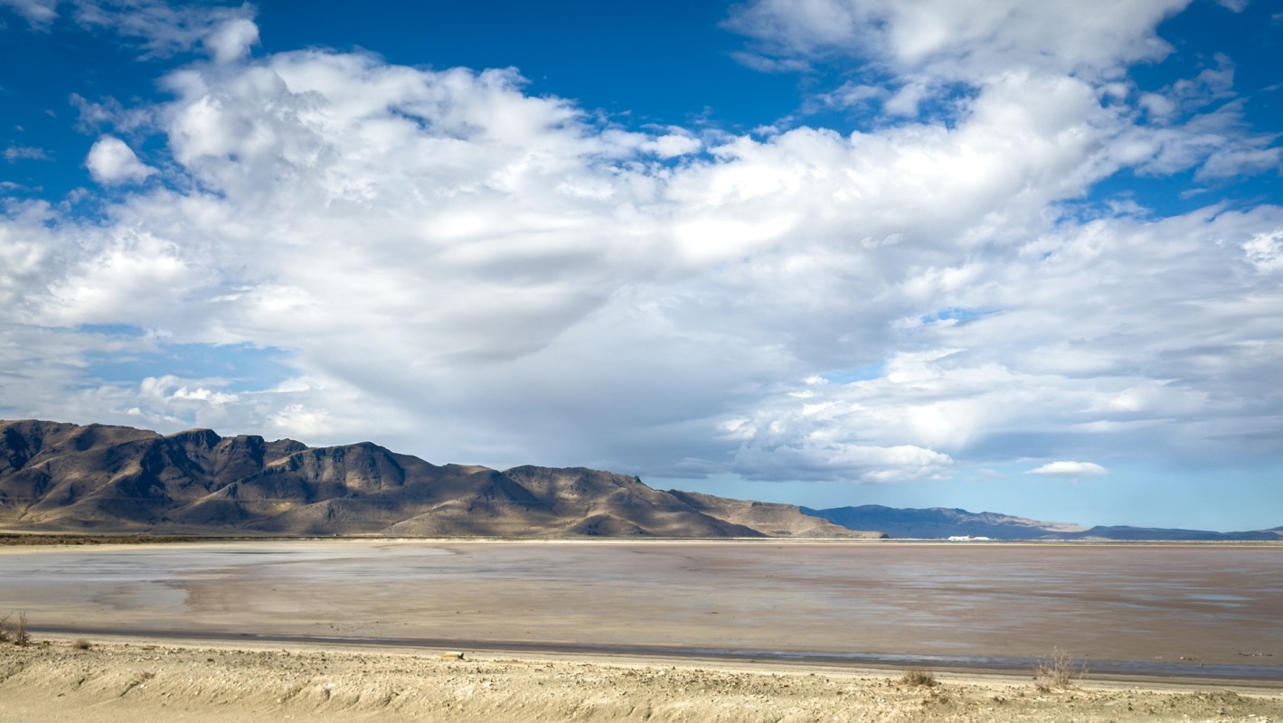 A vast landscape featuring a dry lakebed with mountains under a partly cloudy sky.