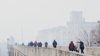 People walking across a bridge in a cityscape filled with smog with buildings barely visible in the background.