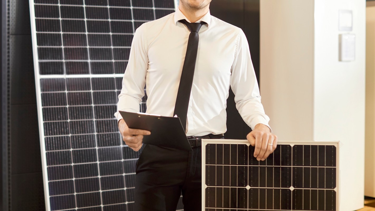 A professional stands with solar panels and a clipboard.