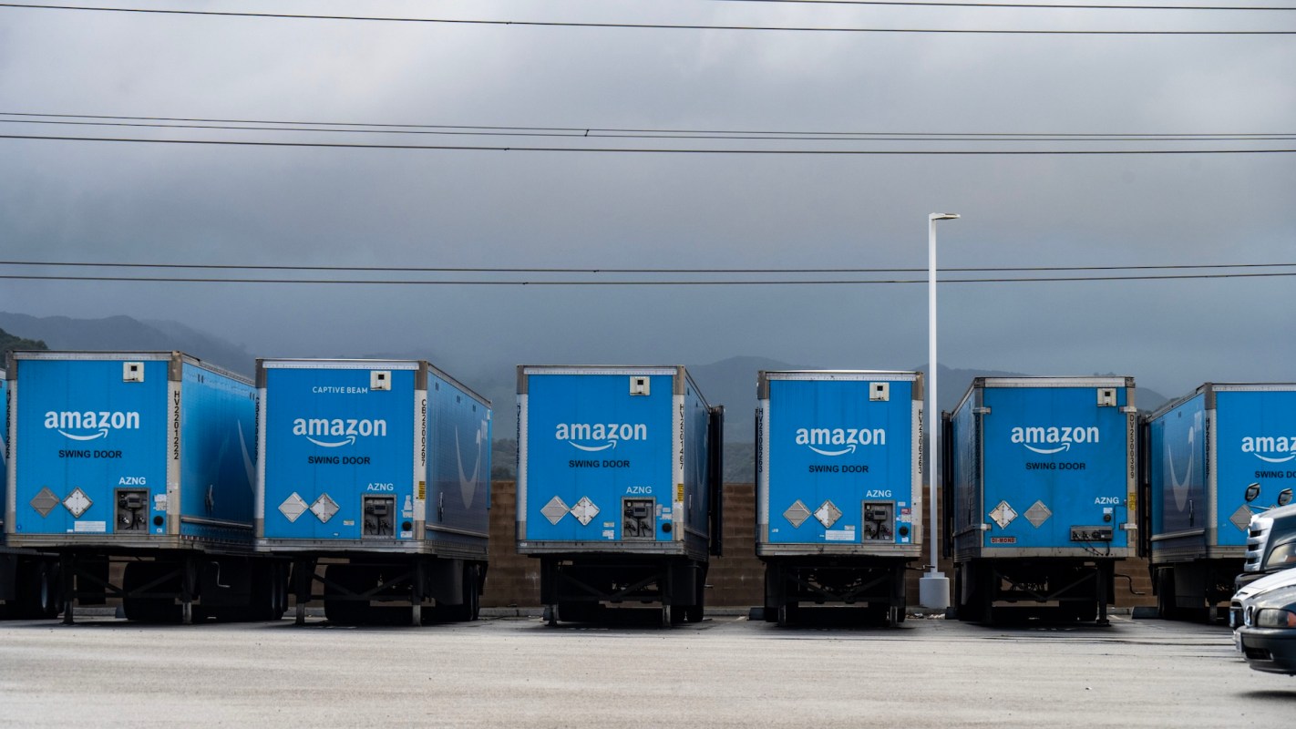 A row of blue Amazon delivery trucks parked in a lot under a cloudy sky.