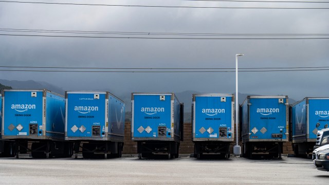 A row of blue Amazon delivery trucks parked in a lot under a cloudy sky.