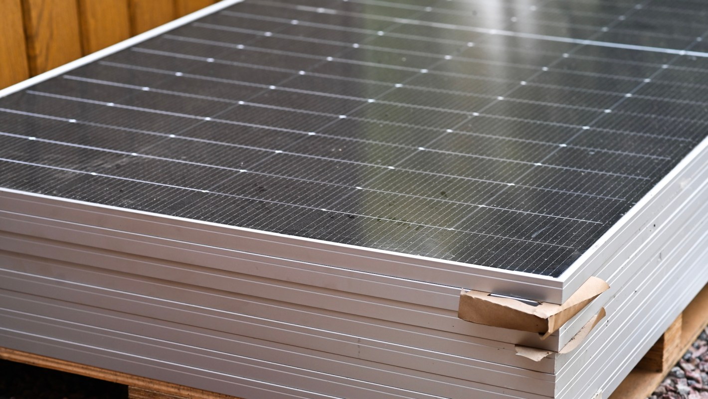 A stack of solar panels resting on a wooden pallet with a wooden background.
